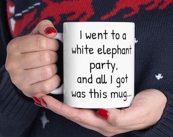 May include: White ceramic mug with the text "I went to a white elephant party, and all I got was this mug..." in black. The mug is held by a person wearing a blue sweater with a red and white pattern.