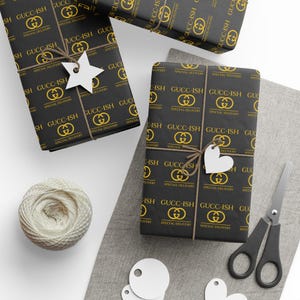 May include: Several wrapped gifts with black and gold patterned paper, tied with twine and adorned with white tags. The paper features the text "GUCC-ISH" and a logo. A ball of twine and scissors are also present.