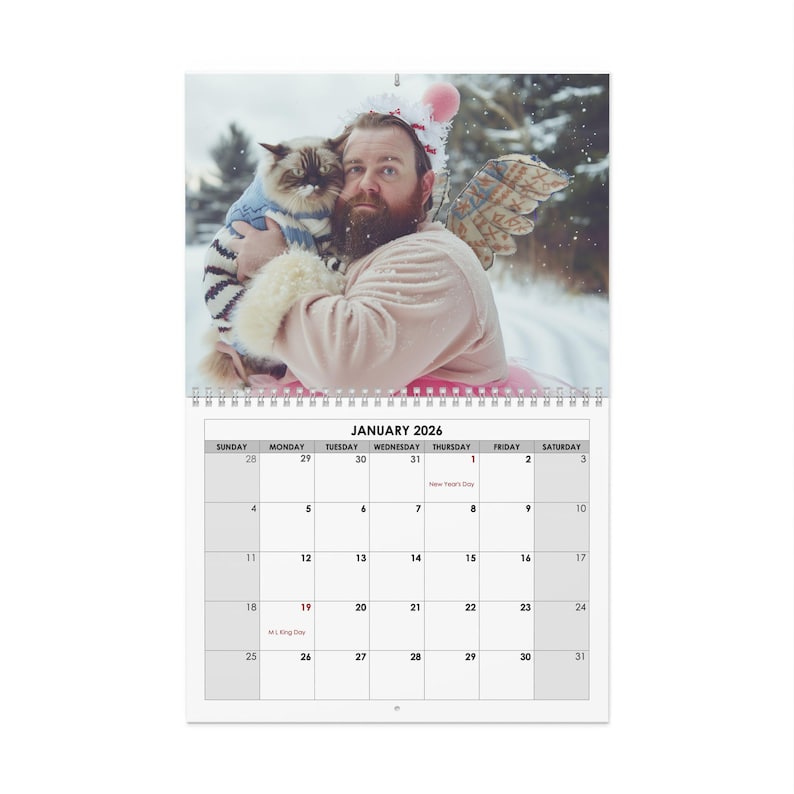 May include: A 2026 wall calendar featuring a whimsical image of a person dressed in a pink outfit with angel wings, holding a cat. The calendar shows the month of January with the days of the week and dates.