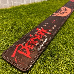 K&ouml;nnte beinhalten: Ein schwarzer Leder-Gewichtheberg&uuml;rtel mit rotem japanischem Text und einer Grafik. Der G&uuml;rtel hat mehrere L&ouml;cher zur Anpassung und der Text "GOLDEN AGE ARC" ist in Wei&szlig; gedruckt. Der G&uuml;rtel liegt auf einer gr&uuml;nen Oberfl&auml;che.