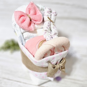 May include: A pink and white baby shower gift basket with a pink bow, a pink and white blanket, and a pink and white stuffed toy. The basket is decorated with pink polka dots and a gold bow.