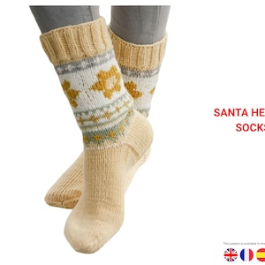 Könnte beinhalten: Cremefarbene Stricksocken mit einem Blumenmuster in Gelb, Weiß und Grau. Die Socken haben einen gerippten Bund und den Text "SANTA HEARTS SOCKS" in Rot. Das Muster ist in mehreren Sprachen verfügbar.
