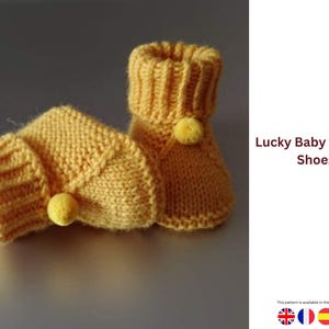 Könnte beinhalten: Ein Paar gestrickte Baby-Booties in einem weichen Gelbton. Jeder Bootie hat einen gerippten Bund und einen kleinen gelben Pompon. Der Text "Lucky Baby Booties Shoes" ist sichtbar.