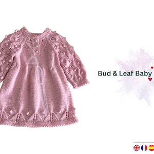 May include: A light pink knitted baby dress with long sleeves. The dress features a textured pattern on the sleeves and hem, with small decorative details. The text "Bud & Leaf Baby Dress" is visible on the right side of the image.