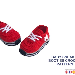Può includere: Due scarpine da neonato all'uncinetto rosse e bianche a forma di sneaker. Le scarpe hanno lacci bianchi, una suola bianca e nera e una lettera "M" bianca sul lato. È visibile anche il testo "BABY SNEAKER BOOTIES CROCHET PATTERN".