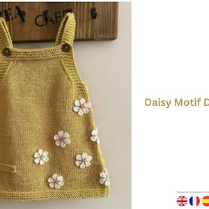 Puede incluir: Vestido de punto amarillo mostaza con aplicaciones de margaritas blancas. El vestido tiene un escote cuadrado, tirantes abotonados y un pequeño bolsillo. El texto "Daisy Motif Dress" se muestra.