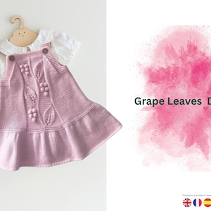 Puede incluir: Un vestido de punto lila con una camisa blanca con cuello debajo, exhibido en una percha de madera con forma de nube. El vestido presenta un diseño de hojas de uva y el texto "Grape Leaves Dress".
