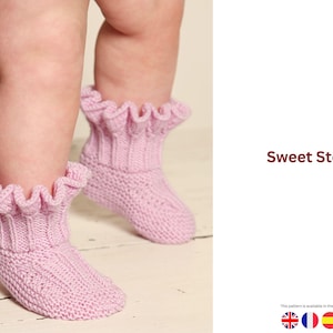 May include: A pair of light pink knitted baby booties with frilled tops. The booties are on a baby's feet, with the text "Sweet Steps" in the image. The booties are a soft, cosy design.