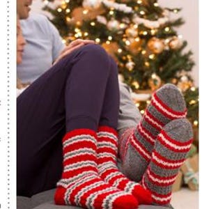 May include: A couple wearing red and gray striped socks with a Christmas tree in the background.