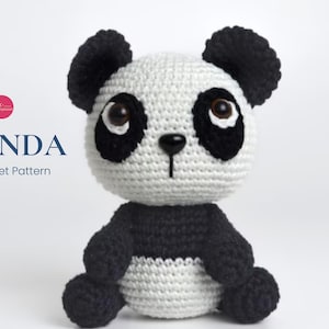May include: A crocheted panda amigurumi toy with black and white fur. The panda has black eyes and a black nose. The toy is sitting on a white background.