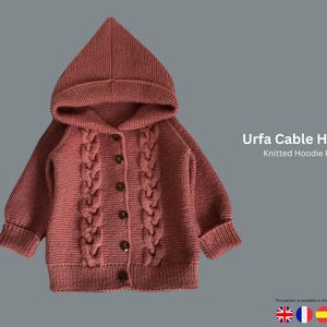 May include: A knitted dusty rose-coloured hoodie featuring a cable knit design on the front. The hoodie has a pointed hood, long sleeves, and a button-up closure. The text "Urfa Cable Hoodie" and "Knitted Hoodie Pattern" are visible.