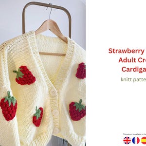 Puede incluir: C&aacute;rdigan color crema con botones, aplicaciones de fresas rojas y hojas verdes. La prenda de punto est&aacute; colgada en una percha de madera. El texto de la derecha dice "Strawberry Motif Adult Crop Cardigan knitt pattern."