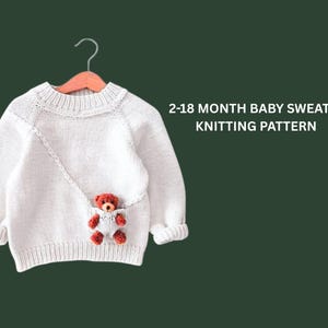 May include: A white baby sweater with a small red teddy bear in a pocket. The sweater is hanging on a wooden hanger against a dark green background. Text on the right says "2-18 MONTH BABY SWEATER KNITTING PATTERN."