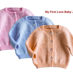 Op de afbeelding: Drie gebreide babyvestjes in roze, blauw en perzik. Elk vestje heeft een ronde hals, lange mouwen en een knoopsluiting. De tekst "My First Love Baby Jacket" staat rechtsboven.