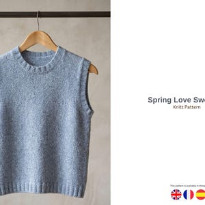 Könnte beinhalten: Eine hellblaue Strickweste hängt an einem Holzbügel. Das ärmellose Kleidungsstück hat einen Rundhalsausschnitt und einen gerippten Saum. Der Text "Spring Love Sweater Knitt Pattern" ist sichtbar.
