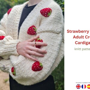 Puede incluir: C&aacute;rdigan de punto grueso color crema adornado con aplicaciones de fresas rojas. El su&eacute;ter corto tiene cuello en V y mangas largas. El texto en la imagen dice "Strawberry Motif Adult Crop Cardigan knitt pattern."