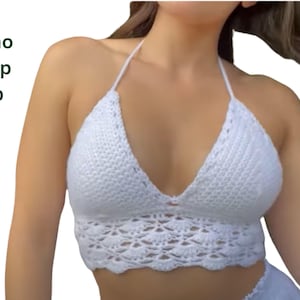 Puede incluir: Top corto blanco de ganchillo con diseño halter. El top presenta un patrón de puntadas texturizadas y un diseño calado decorativo en el borde inferior. El texto "Boho Crop Top" es visible.