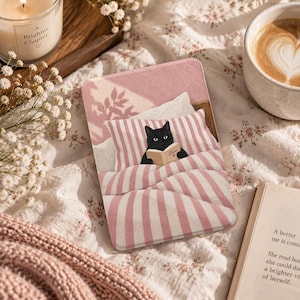 May include: A rectangular e-reader case featuring a graphic illustration of a black cat lying in a bed with pink and white striped bedding. The cat is holding a small open book with the name Oliver printed on the cover. The design includes a soft pink background with a subtle floral shadow pattern.