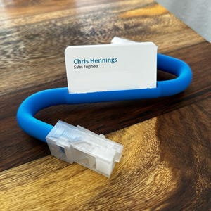 May include: A blue plastic business card holder with a white business card that reads "Chris Hennings, Sales Engineer".