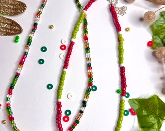 May include: Two beaded necklaces with red, green, and white beads. One necklace has a small green Christmas tree charm, and the other has a white snowflake charm.
