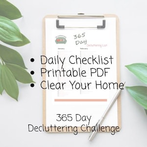 Pode incluir: Uma prancheta com uma lista de desapego de 365 dias impressa, uma caneta e plantas verdes com folhas. A lista inclui o texto "Daily Checklist", "Printable PDF" e "Clear Your Home". O título diz "365 Day Decluttering Challenge."