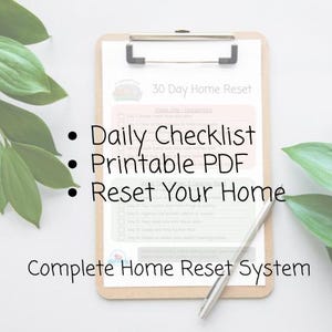 May include: A clipboard with a 30-day home reset checklist, a silver pen, and green leafy plants. The checklist includes the text "Daily Checklist," "Printable PDF," and "Reset Your Home." The phrase "Complete Home Reset System" is also visible.