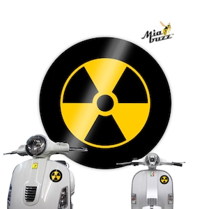 May include: A large black and yellow radiation symbol sticker. Two white scooters are in the foreground, each with a smaller radiation symbol sticker. The Mia Buzz logo is in the upper right corner.