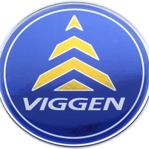 May include: A round, blue emblem with a silver border. The emblem features a yellow arrow design and the word "VIGGEN" in white text. The design is centered on the emblem.