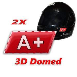 Pode incluir: Dois adesivos 3D abobadados vermelhos com letras brancas A+. Os adesivos são mostrados em um capacete de motocicleta preto.