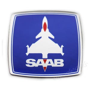 Könnte beinhalten: Ein blau-weißes Saab-Emblem mit einem Düsenflugzeug-Design. Das Emblem hat ein weißes Düsenflugzeug in der Mitte mit roten Akzenten und das Wort "SAAB" in weißen Buchstaben am unteren Rand. Das Emblem ist vor blauem Hintergrund.