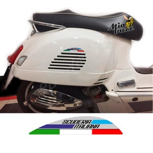 Könnte beinhalten: Ein weißer Roller mit schwarzem Sitz und Chromdetails. Der Roller hat ein "Mia Buzz"-Logo und einen "Scuderia Italiana"-Aufkleber. Die Seitenwand hat horizontale schwarze Lüftungsschlitze.