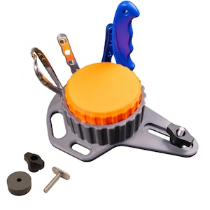 May include: A gray plastic base with a circular orange top and a ridged edge, featuring a blue handle, a silver metal tool, and a pair of silver scissors. A separate black knob, a small gray cylinder, and a metal bolt are positioned nearby.