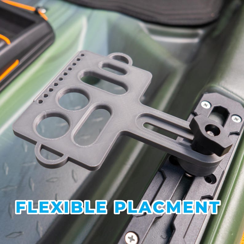 Puede incluir: Un soporte de accesorios gris de pl&aacute;stico para kayak, con una placa plana que presenta m&uacute;ltiples recortes circulares y alargados, fijado a un sistema de riel negro con una perilla de ajuste. El texto "FLEXIBLE PLACMENT" es visible abajo.