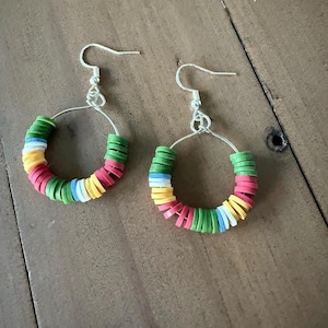 May include: A pair of hoop earrings with colorful, stacked disc beads. The earrings feature a silver-tone hook and a circular design. The beads are in shades of red, yellow, green, blue, and white, creating a vibrant, eye-catching accessory.