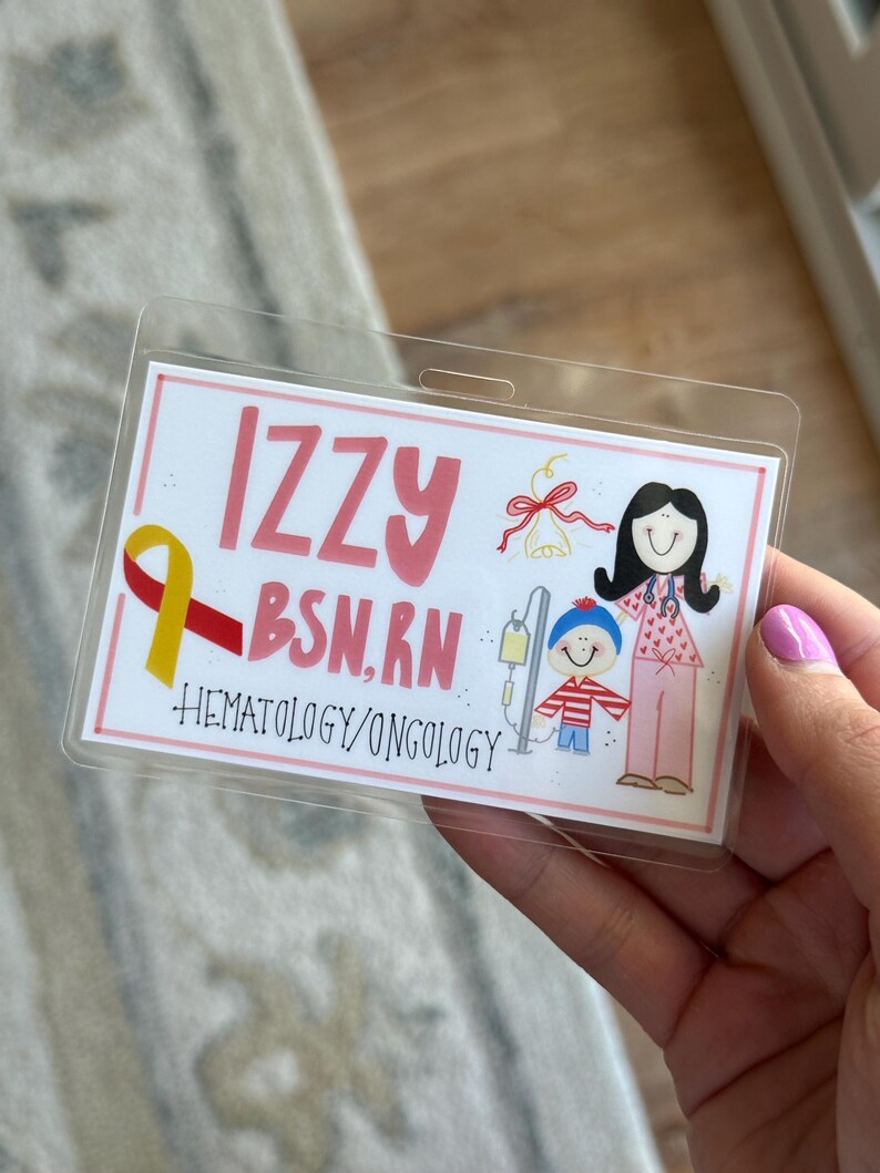 May include: A pink and white ID badge with the name "Izzy BSN, RN" and the text "Hematology/Oncology". The badge features a cartoon illustration of a woman in a pink dress and a child in a red and white striped shirt.