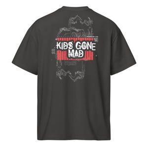 Puede incluir: Camiseta gris oscuro con el texto "KIDS GONE MAD" en blanco y rojo, con un diseño gráfico estilizado en la espalda. La camiseta tiene cuello redondo y mangas cortas. El diseño incluye la palabra "MAD" repetida.