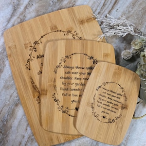 May include: A set of four bamboo cutting boards. Each board has a different size and shape. The boards have a light brown color and feature a floral wreath design with text that reads "Always throw spilled salt over your left shoulder..."