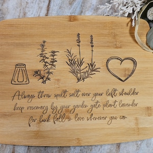 Op de afbeelding: Een rechthoekige bamboe snijplank met lasergegraveerde illustraties van een zoutvaatje, een takje rozemarijn, een lavendelstengel en een hart. De tekst luidt: Always throw spilt salt over your left shoulder keep rosemary by your garden gate plant lavender for luck fall in love wherever you can.