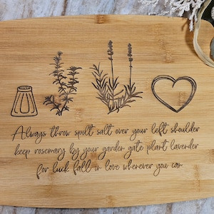 Op de afbeelding: Een rechthoekige bamboe snijplank met lasergegraveerde illustraties van een zoutvaatje, een takje rozemarijn, een lavendelstengel en een hart. De tekst luidt: Always throw spilt salt over your left shoulder keep rosemary by your garden gate plant lavender for luck fall in love wherever you can.