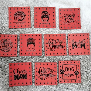 May include: Ten red leather patches with various sayings and designs. The patches have a dotted border and are decorated with rhinestones. Some of the sayings include "Wine Diva", "Fur Mama", "Baseball Mom", and "Cheer Mom".