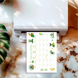May include: A printed calendar page for March 2026, featuring a St. Patrick's Day theme. The calendar has green and yellow illustrations of leprechauns, shamrocks, and rainbows. The calendar is being printed from a white printer.