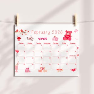 May include: A white Valentine's Day themed calendar for February 2026, hanging from a string with wooden clips. The calendar features pink illustrations of hearts, teddy bears, and cupcakes. The days of the week are listed, with Valentine's Day marked on the 14th.