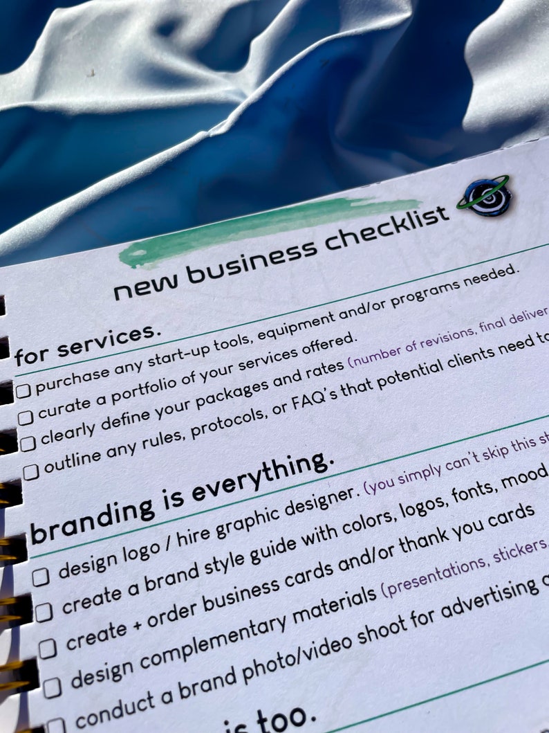 Pode incluir: Um caderno espiralado com uma lista de verifica&ccedil;&atilde;o intitulada "New Business Checklist". A lista de verifica&ccedil;&atilde;o inclui se&ccedil;&otilde;es para servi&ccedil;os e branding, com caixas de sele&ccedil;&atilde;o ao lado de cada item. O caderno est&aacute; em uma superf&iacute;cie azul.