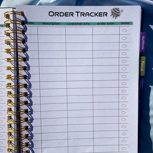 Pode incluir: Um caderno aberto com espiral com as palavras "ORDER TRACKER" impressas no topo. O caderno tem uma encaderna&ccedil;&atilde;o em espiral dourada e cont&eacute;m p&aacute;ginas pautadas com colunas para detalhes do pedido. Abas rotuladas como "outlook" e "focus" s&atilde;o vis&iacute;veis.
