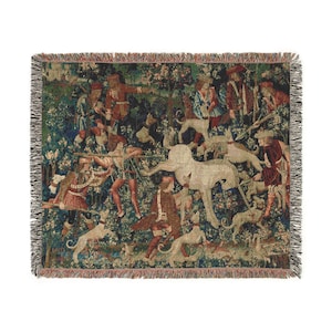 May include: A tapestry woven throw blanket featuring a detailed depiction of a unicorn being hunted by a group of men and dogs in a lush forest setting. The unicorn is white with a golden horn, and the men are dressed in medieval clothing. The tapestry is a vibrant mix of colors, including greens, blues, reds, and yellows.