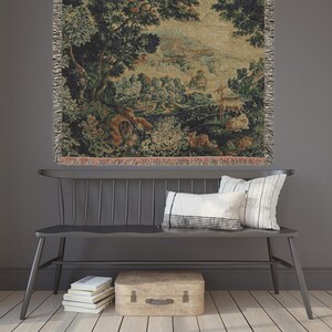 May include: A tapestry wall hanging with a forest scene featuring a deer, rabbits, and other animals. The tapestry is framed by a black wooden bench with two pillows.