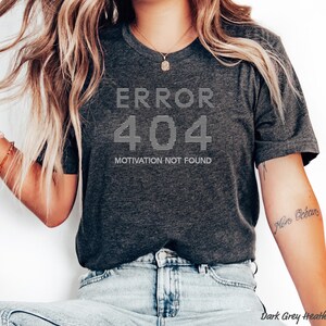 Może przedstawiać: Koszulka w kolorze ciemnoszary melanż z białym napisem "ERROR 404 MOTIVATION NOT FOUND".