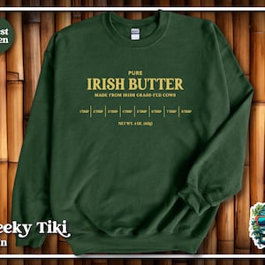 May include: A forest green sweatshirt with the text "PURE IRISH BUTTER MADE FROM IRISH GRASS-FED COWS" in yellow. The text "1 TBSP 2 TBSP 3 TBSP 4 TBSP 5 TBSP 6 TBSP 7 TBSP 8 TBSP" is printed below the main text. The text "NET WT. 4 OZ. (113G)" is printed below the tablespoons.
