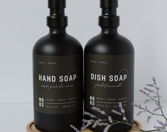 May include: Two black pump bottles with labels for hand soap and dish soap. The bottles are on a wooden tray with purple flowers in the foreground. The hand soap label reads "No. 02" and the dish soap label reads "No. 03". Both bottles are 16.9 fl oz / 500 ml.