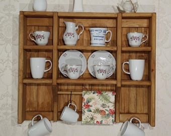 May include: A wooden shelf unit displaying various white ceramic teacups, mugs, and a small teapot. Some cups have floral designs. A small white vase with dried flowers and a decorative light fixture are also visible.